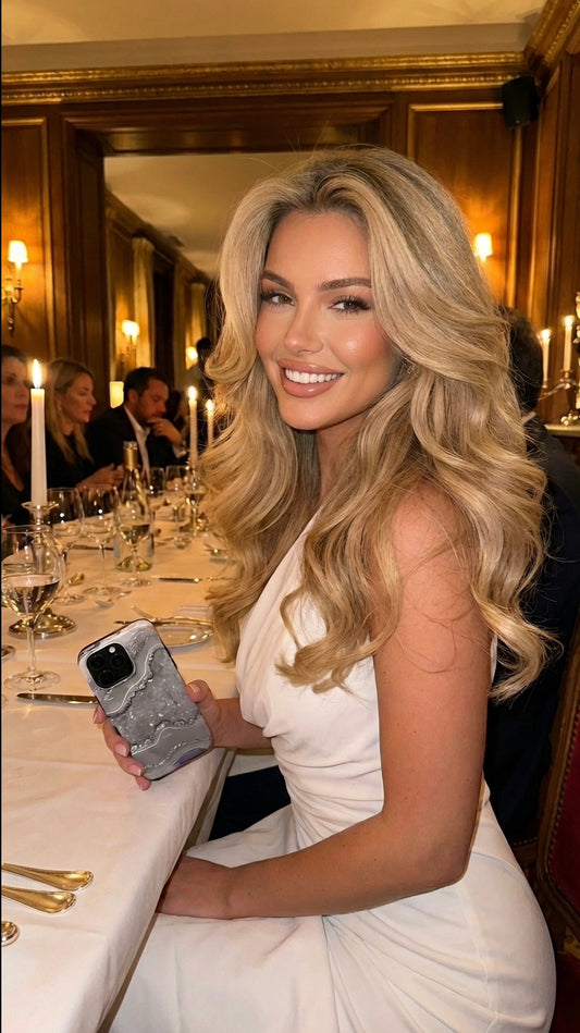Stylish blonde woman at elegant dinner holding a phone with a Sølv, Gråt, Flerfarvet silver marble quartz patterned case, radiant and feminine vibe.