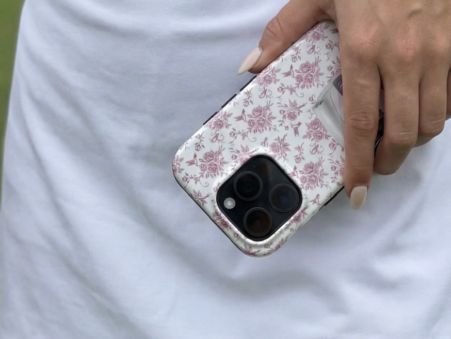 Hand holding a trendy phone case with a feminine pink and white floral flerfarvet pattern against a soft white background, reflecting a girly, aesthetic style.