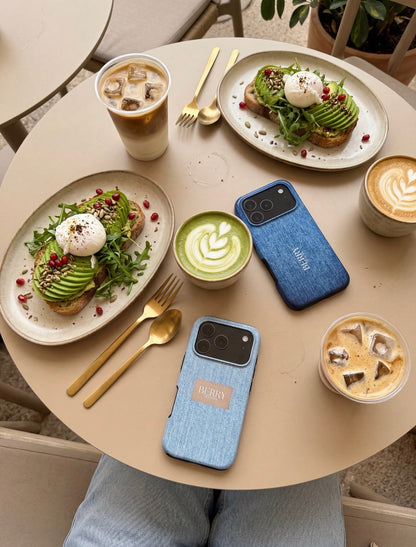 Two plates with avocado toast topped with poached eggs and pomegranate seeds on a beige table with iced coffee, latte, matcha, and two blue phone cases.
