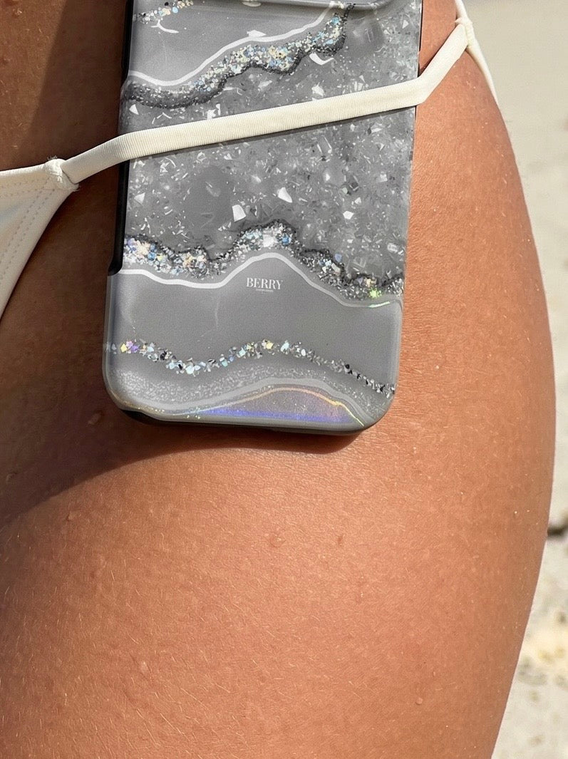 Trendy phone case with silver, gray, and multicolored marble quartz design resting on tanned skin, exuding feminine and aesthetic summer vibes.