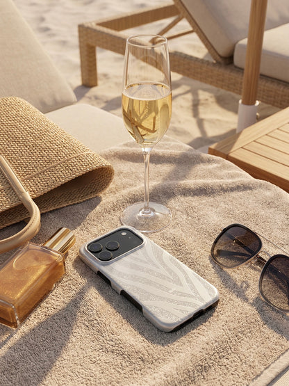 Trendy phone case with gray and silver zebra pattern on a beach towel alongside stylish sunglasses, a glass of champagne, and a straw bag for a feminine, chic vibe.
