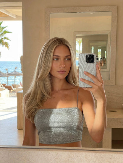 Trendy woman with long blonde hair taking a mirror selfie holding a phone with a gray and silver zebra-patterned case in a bright, stylish room by the beach.
