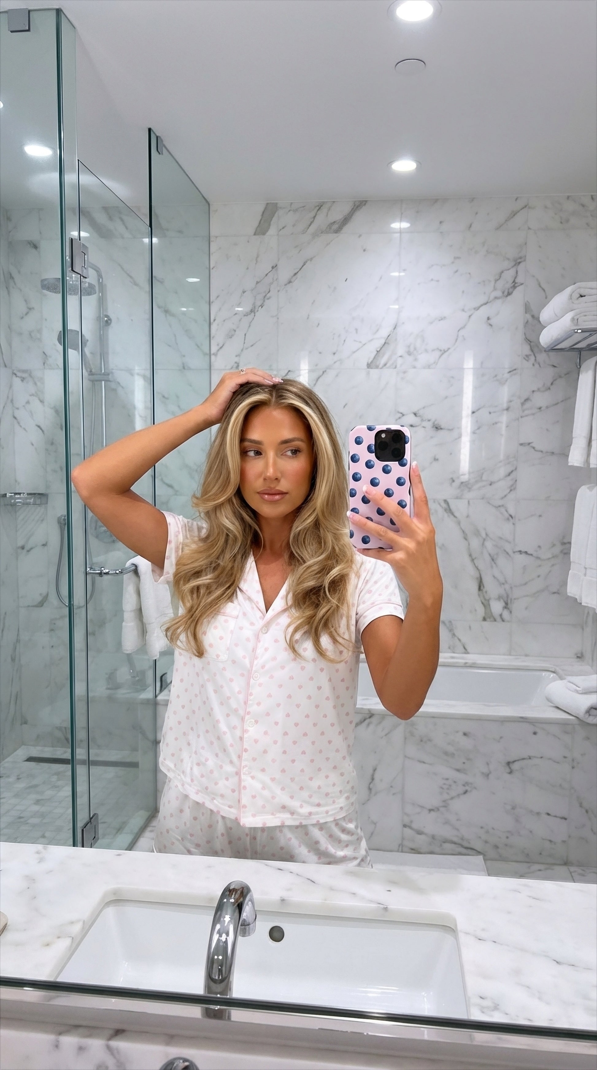 Trendy feminine phone case with pink and blue blueberry pattern held by a stylish woman in a bright, modern bathroom mirror selfie.