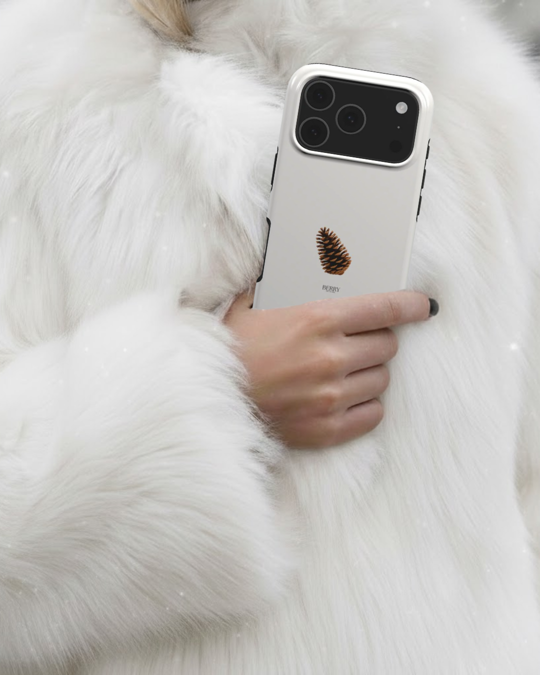 Hand holding a trendy phone case in beige with a brun and flerfarvet pine cone design, styled with a luxurious white furry coat.