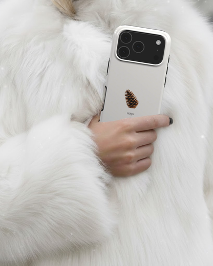 Hand holding a trendy phone case in beige with a brun and flerfarvet pine cone design, styled with a luxurious white furry coat.